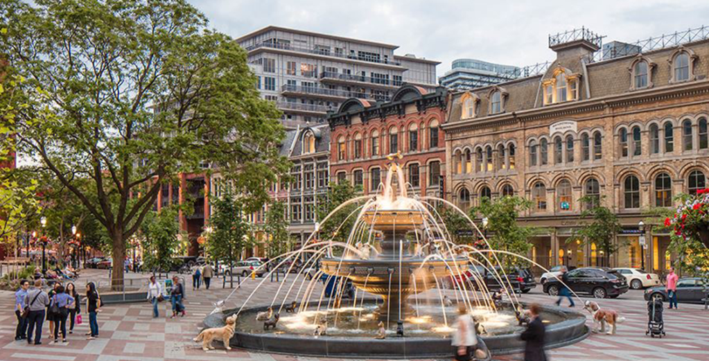 The multi-level water fountain at Berczy Park in Toronto features many artificial dogs looking up at a bone on top of the fountain. 